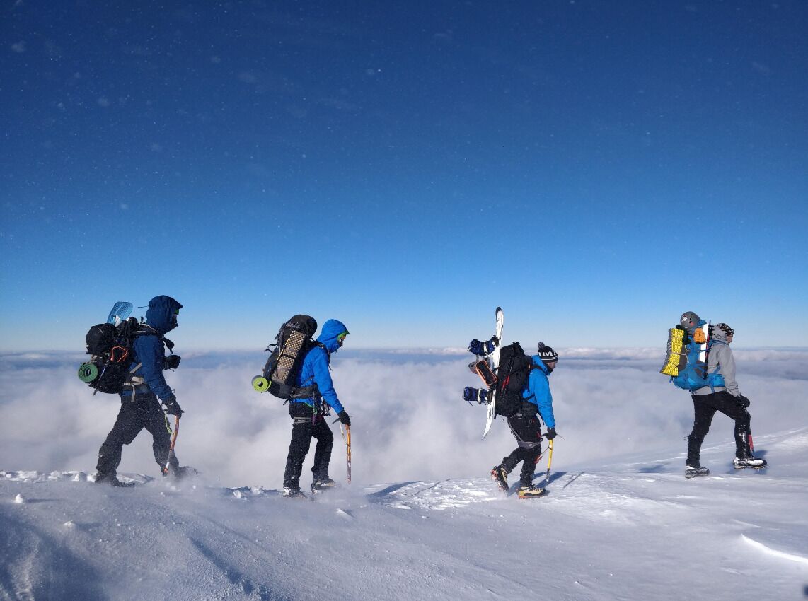 A group of people hiking on a snowy mountain with clear skies.