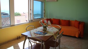 A dining area with a table, chairs, a vase with flowers, and a sofa with orange cushions.