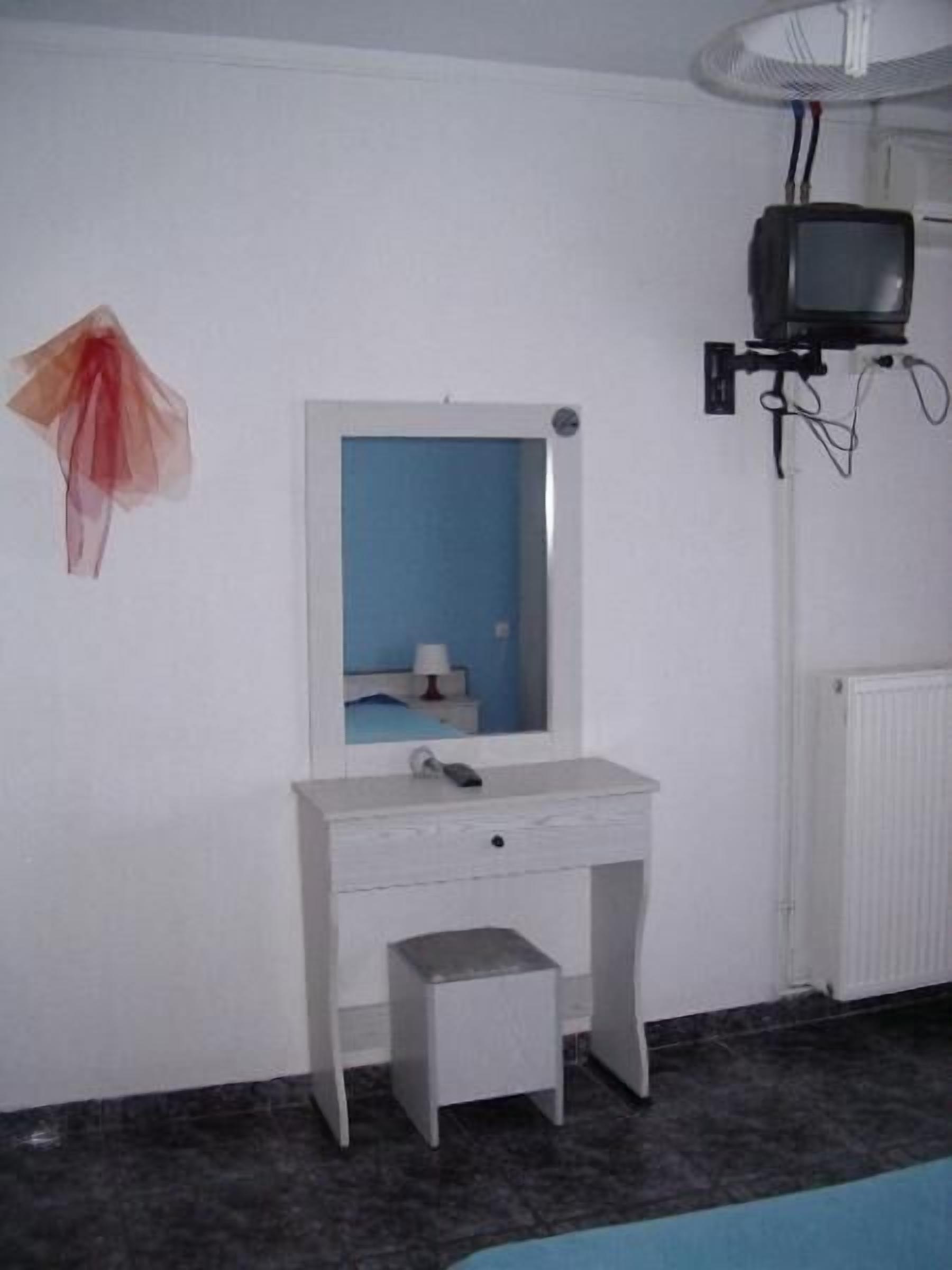 A room with a white desk, a small stool, a mirror, and a television mounted on the wall.
