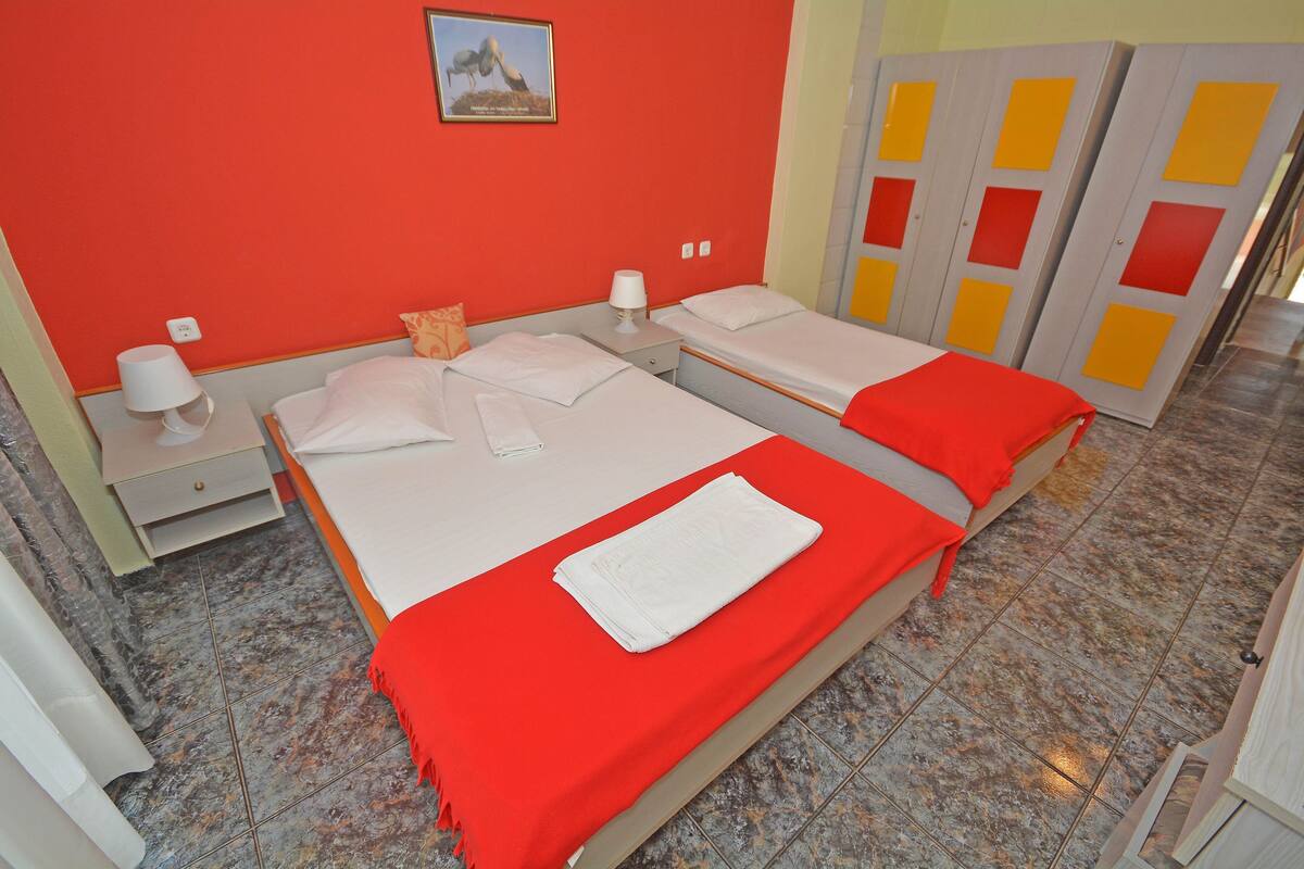 Hotelkamer met twee bedden, een kleurencombinatie van rood en wit, een marmeren vloer en een foto aan de muur.