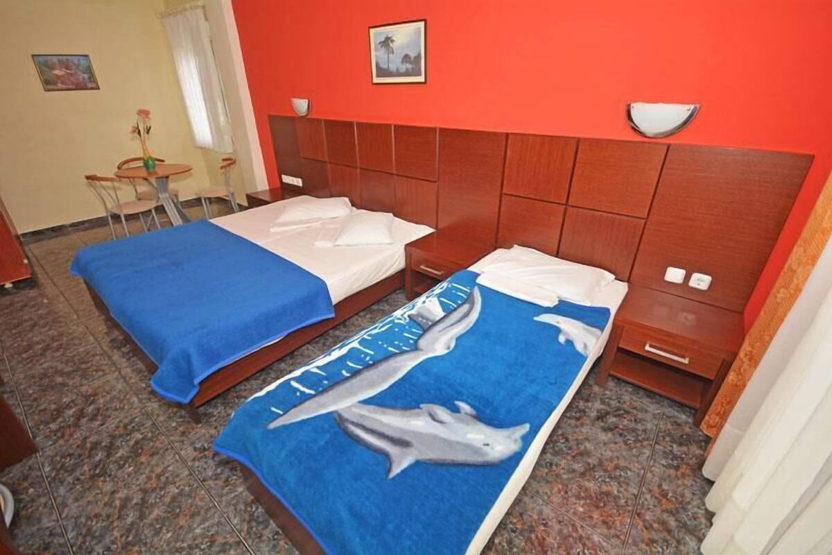 Een hotelkamer met twee bedden, een houten hoofdbord, een tafeltje met stoelen en een schilderij aan de muur.