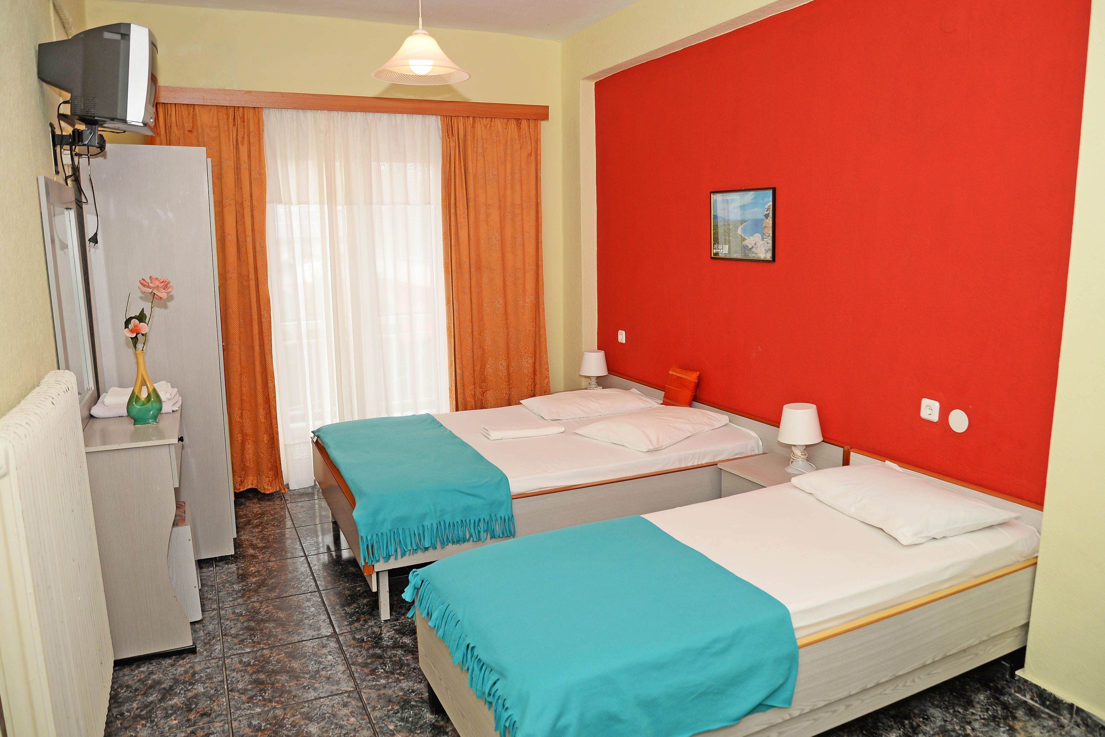 A hotel room with two beds, a TV, a desk, and a window with curtains.