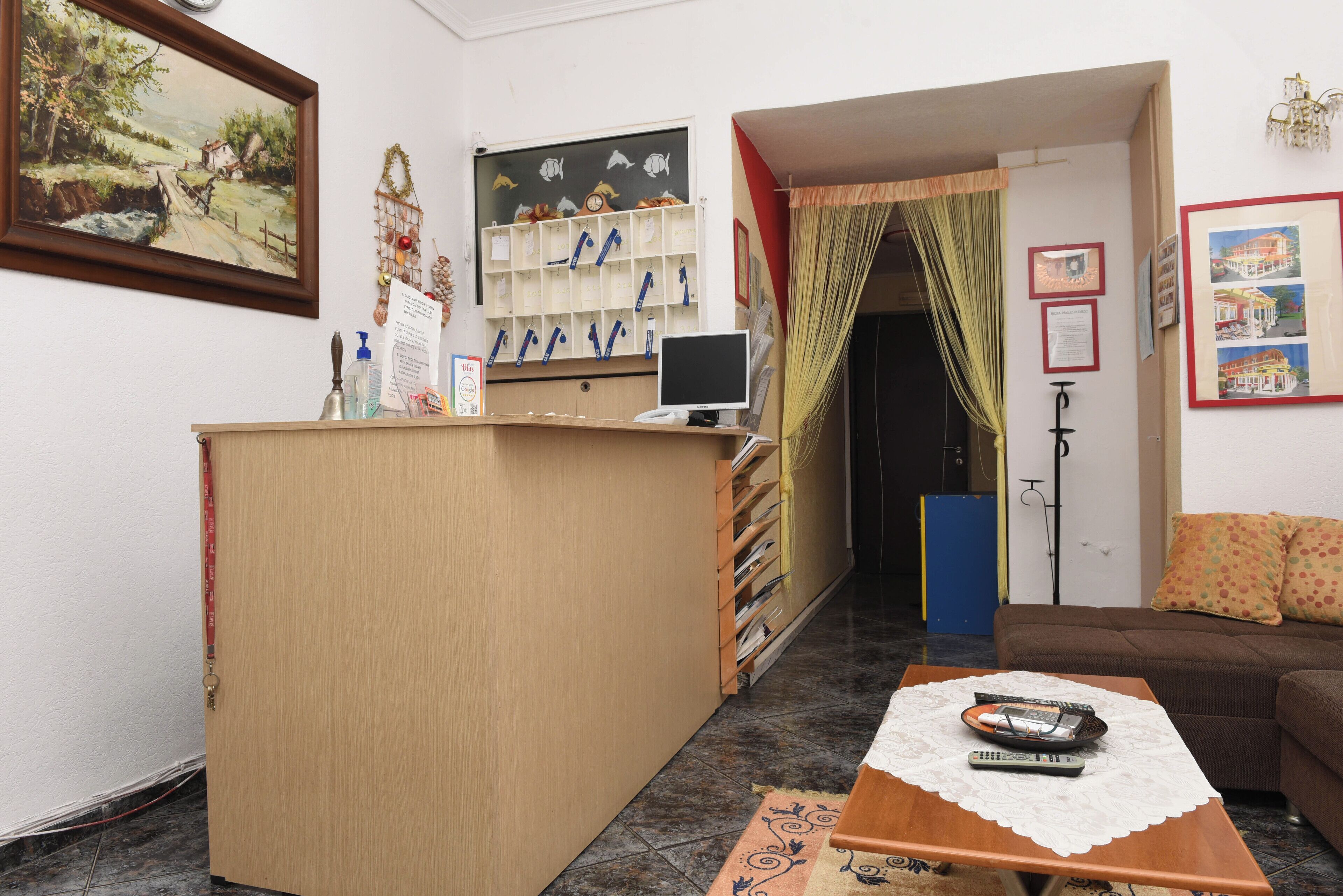A reception area with a wooden desk, a computer, and a couch. There are framed pictures on the wall and a painting above the desk.