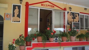 A reception area with a red and yellow facade, potted plants, and a staircase leading to an upper level with white chairs.