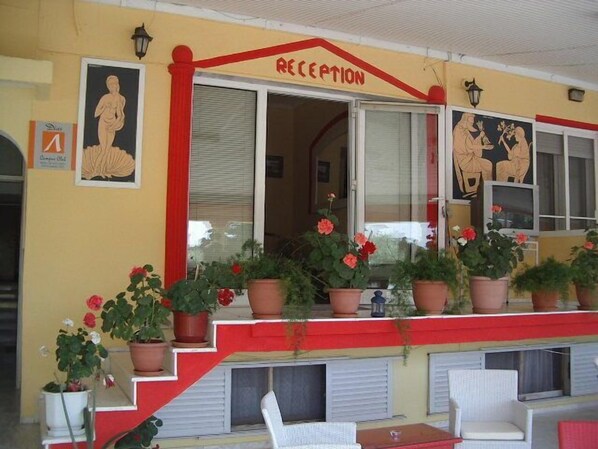 A reception area with a red and yellow facade, potted plants, and a staircase leading to an upper level with white chairs.