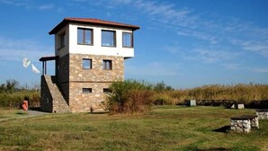 A two-story stone building with a red-tiled roof, a small balcony, and a staircase leading to the upper floor.