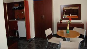 A compact kitchen with a refrigerator, a dining table with four chairs, and a small cabinet with a mirror above it.