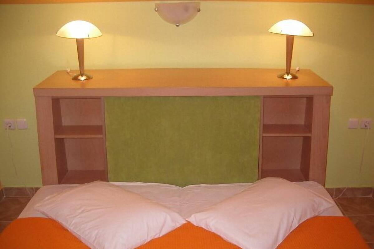 Een bed met twee kussens, een groen hoofdeinde en twee wandlampen.