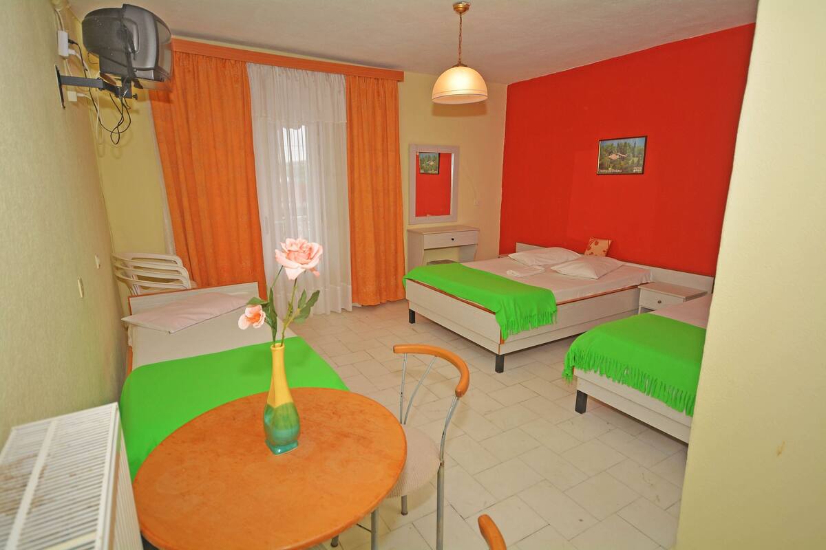 Een hotelkamer met twee bedden, een eettafel met stoelen, een klein bureau en een aan de muur bevestigde televisie.