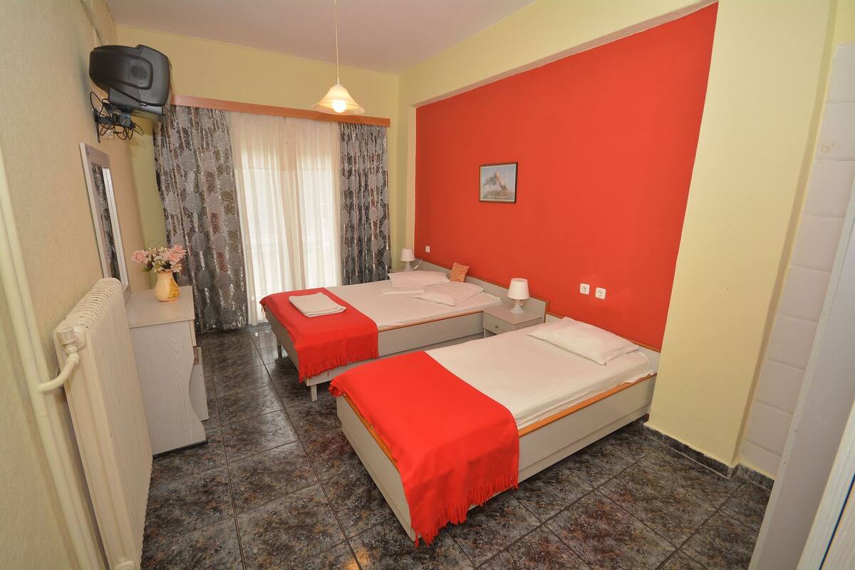 Een kamer met twee bedden, een radiator, een televisie en een raam met gordijnen.
