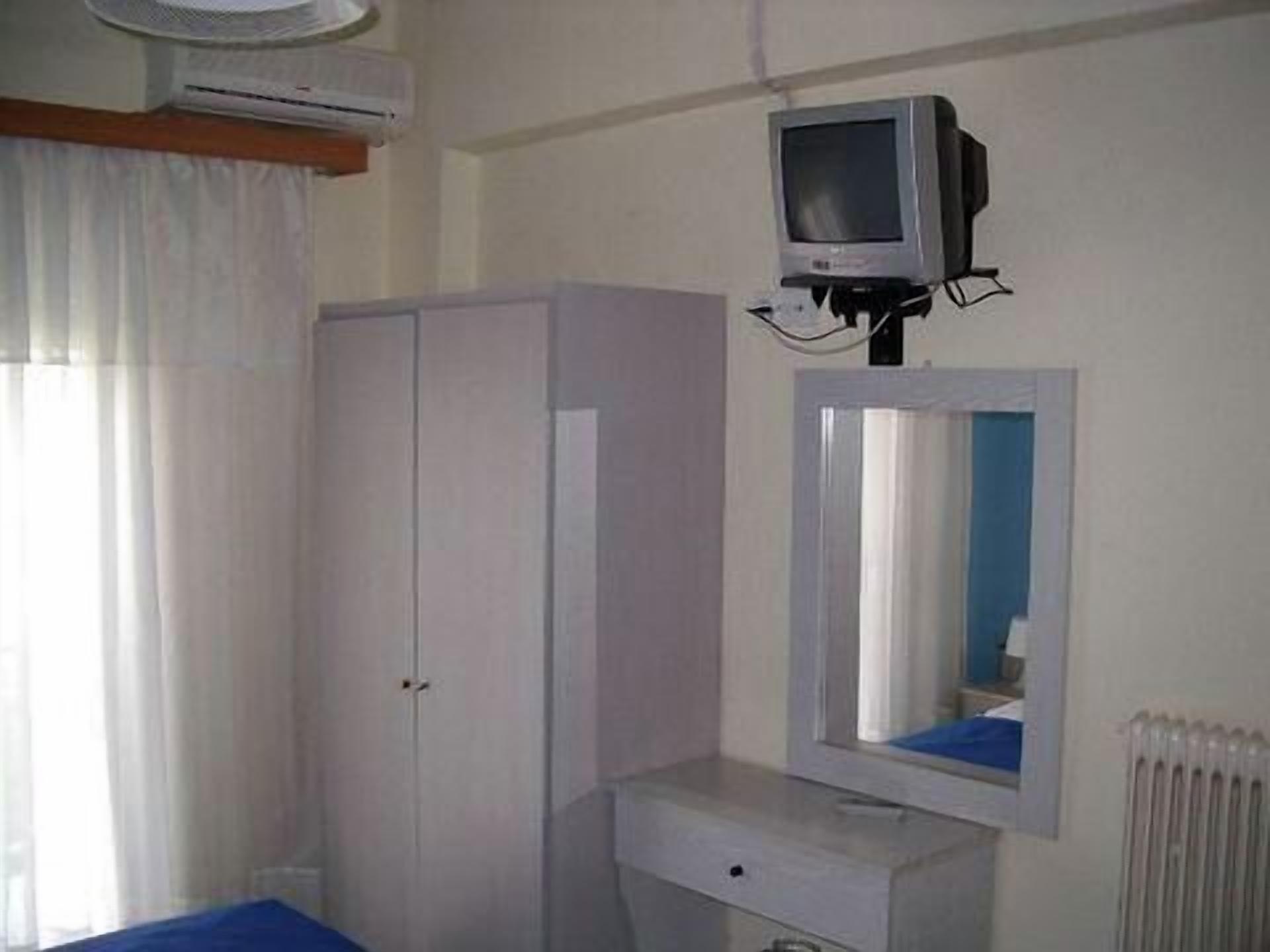 A bedroom with a single bed, a wardrobe, a small desk, a mirror, and a television mounted on the wall.