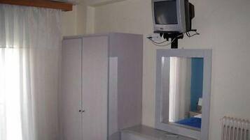 A bedroom with a single bed, a wardrobe, a small desk, a mirror, and a television mounted on the wall.
