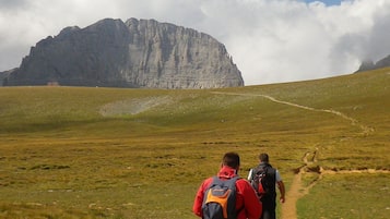Dos excursionistas en un sendero cubierto de hierba, con una montaña al fondo.