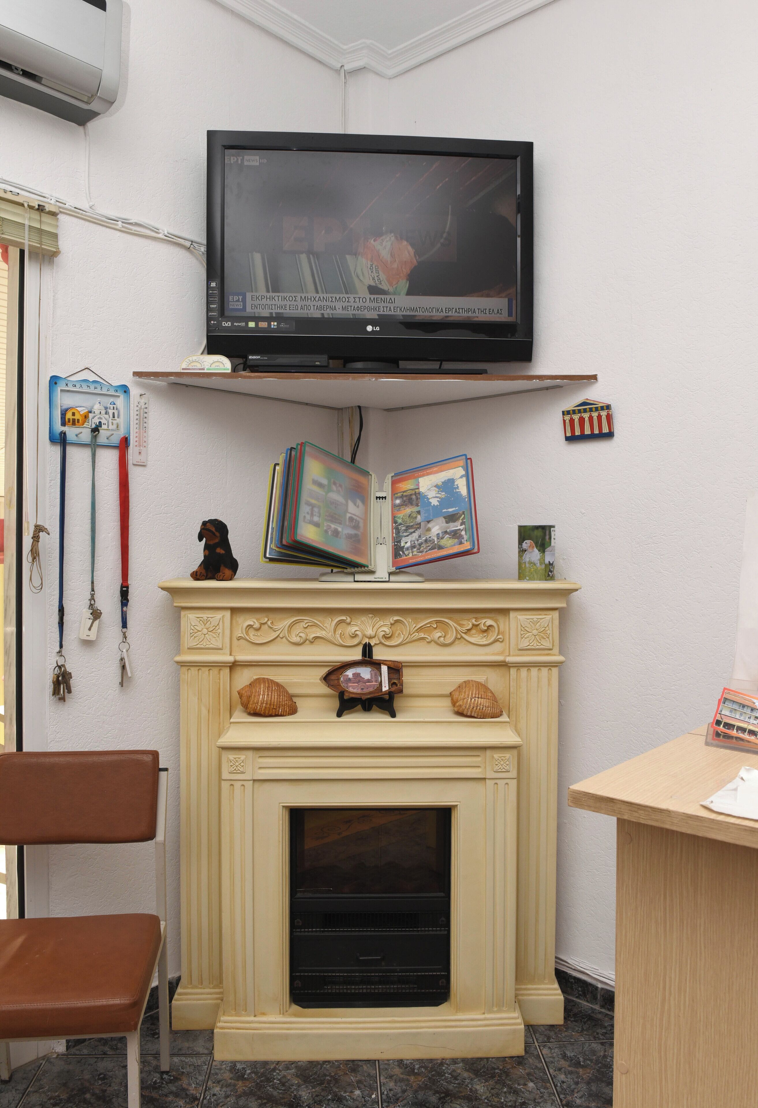 A room with a television mounted above a fireplace, a chair, and a desk with a lamp.