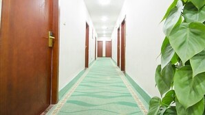 A hotel hallway with wooden doors, a patterned carpet, and a potted plant. - Greentree Inn Fujian Xiamen University Business Hotel (Xiamen)