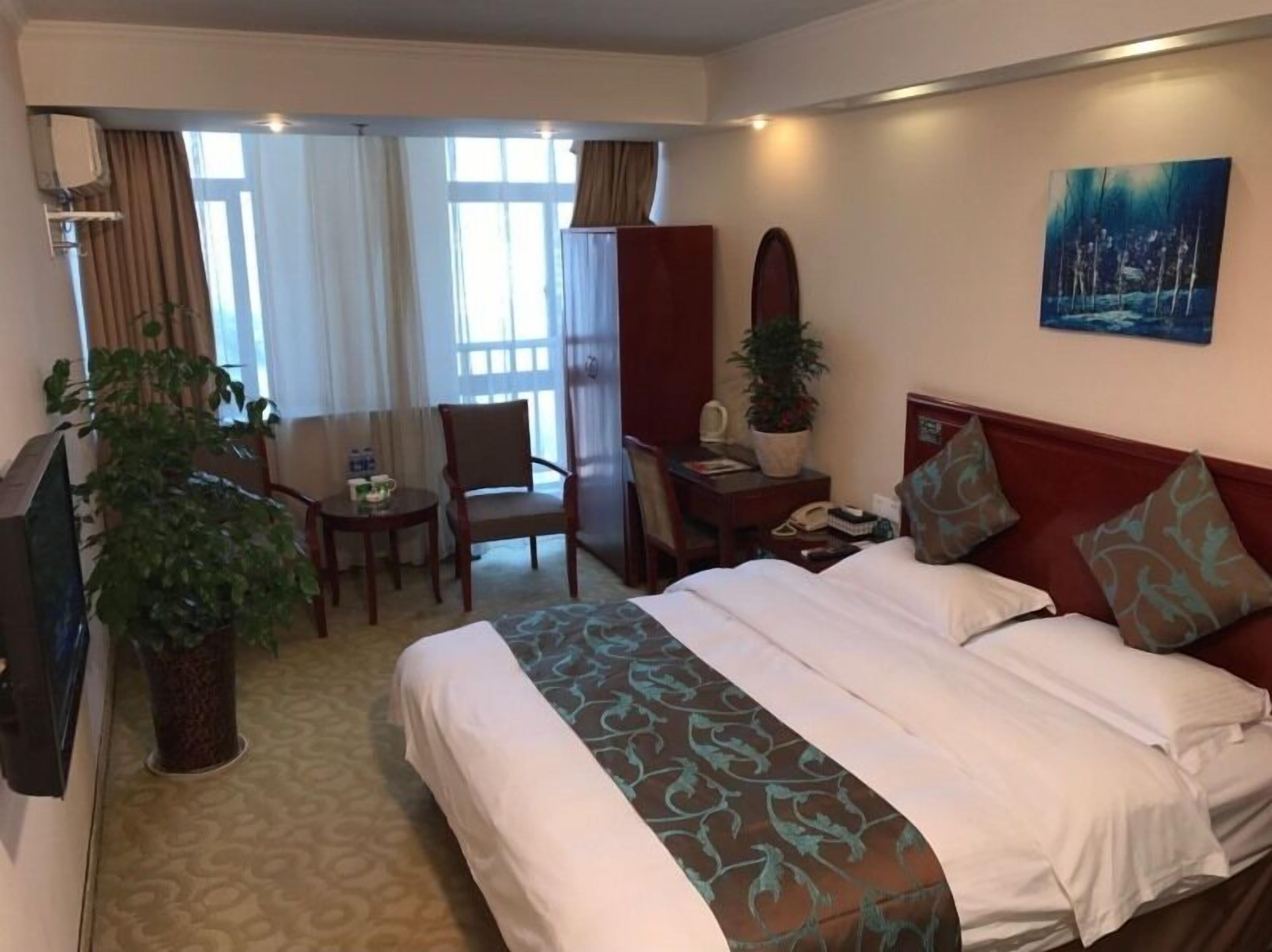 Habitación de hotel con cama, escritorio, silla, televisor y ventana grande.
