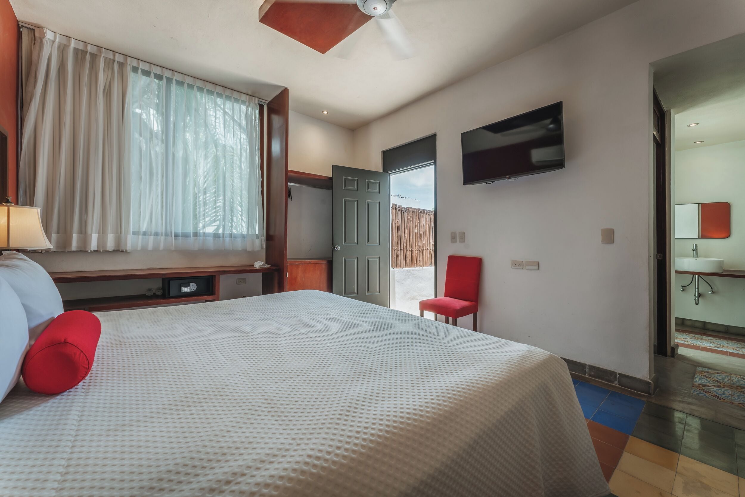 A hotel room with a bed, a TV, a red chair, and a bathroom visible through an open door.