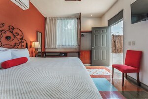 Ein Hotelzimmer mit Bett, einem roten Sessel, einem Fernseher, einem Kleiderschrank und einem Fenster mit Vorhängen.
