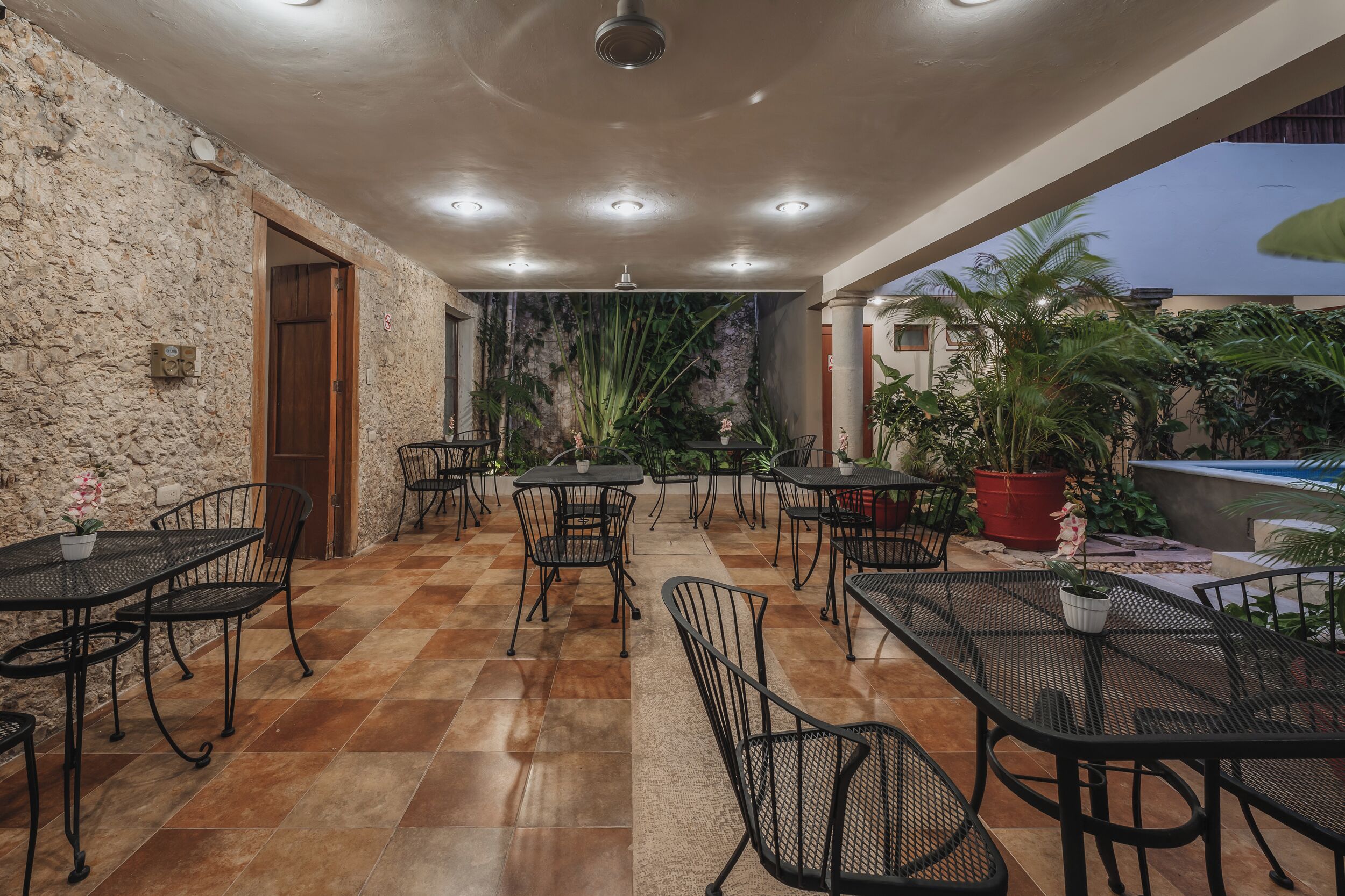 An outdoor patio area with multiple tables and chairs, a stone wall, and potted plants.