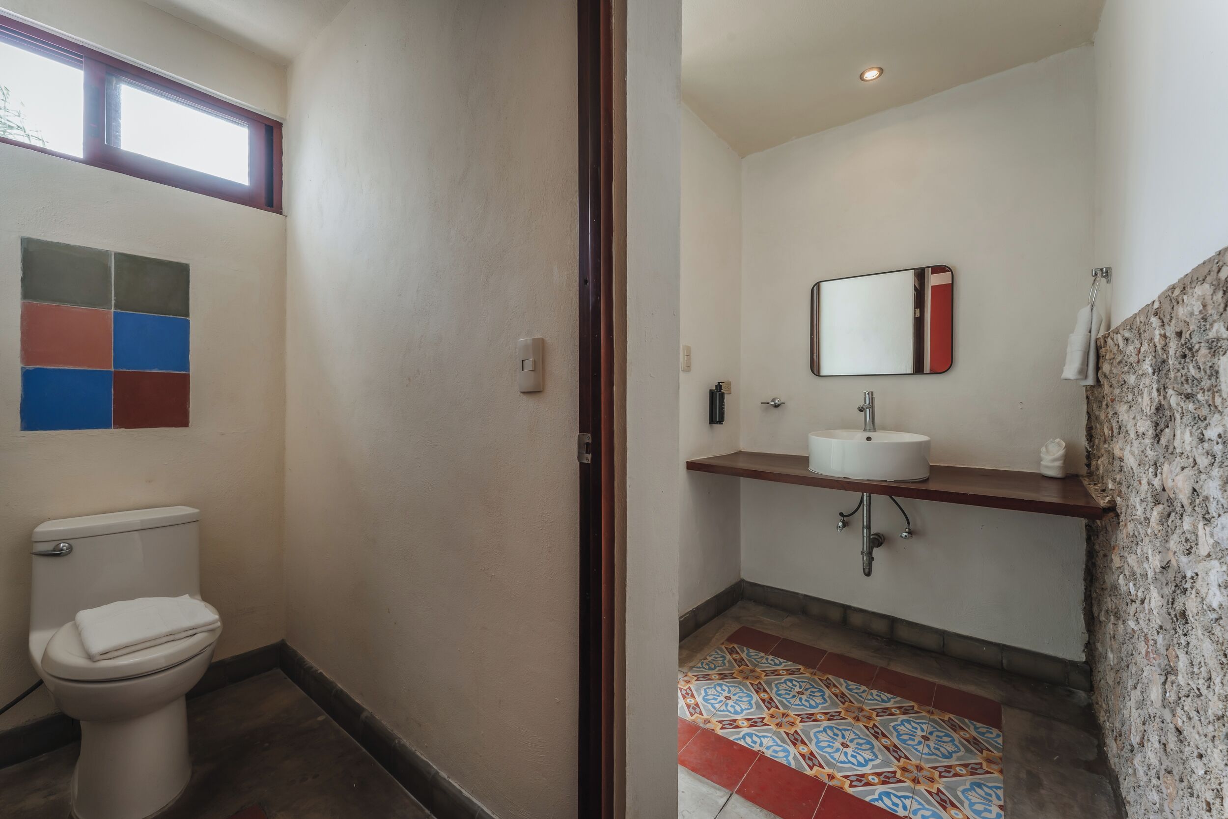 A bathroom with a toilet, sink, mirror, and colorful patterned floor tiles.