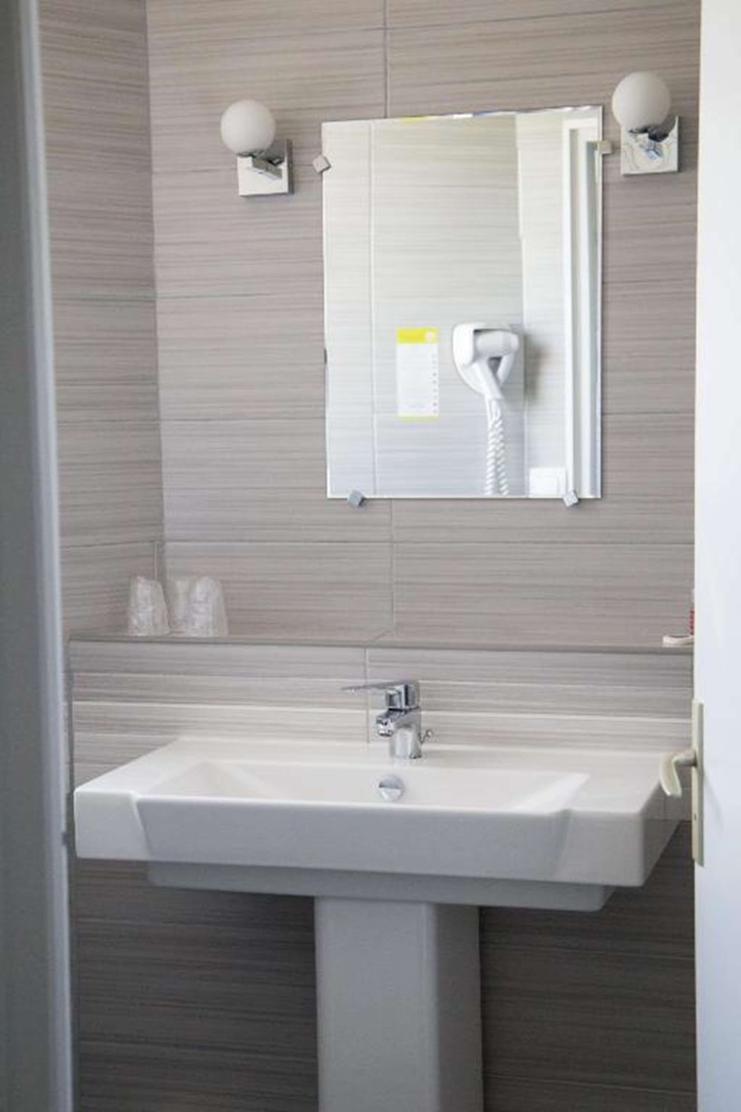 Un baño con un lavamanos blanco, un espejo y dos luces fijadas a la pared.