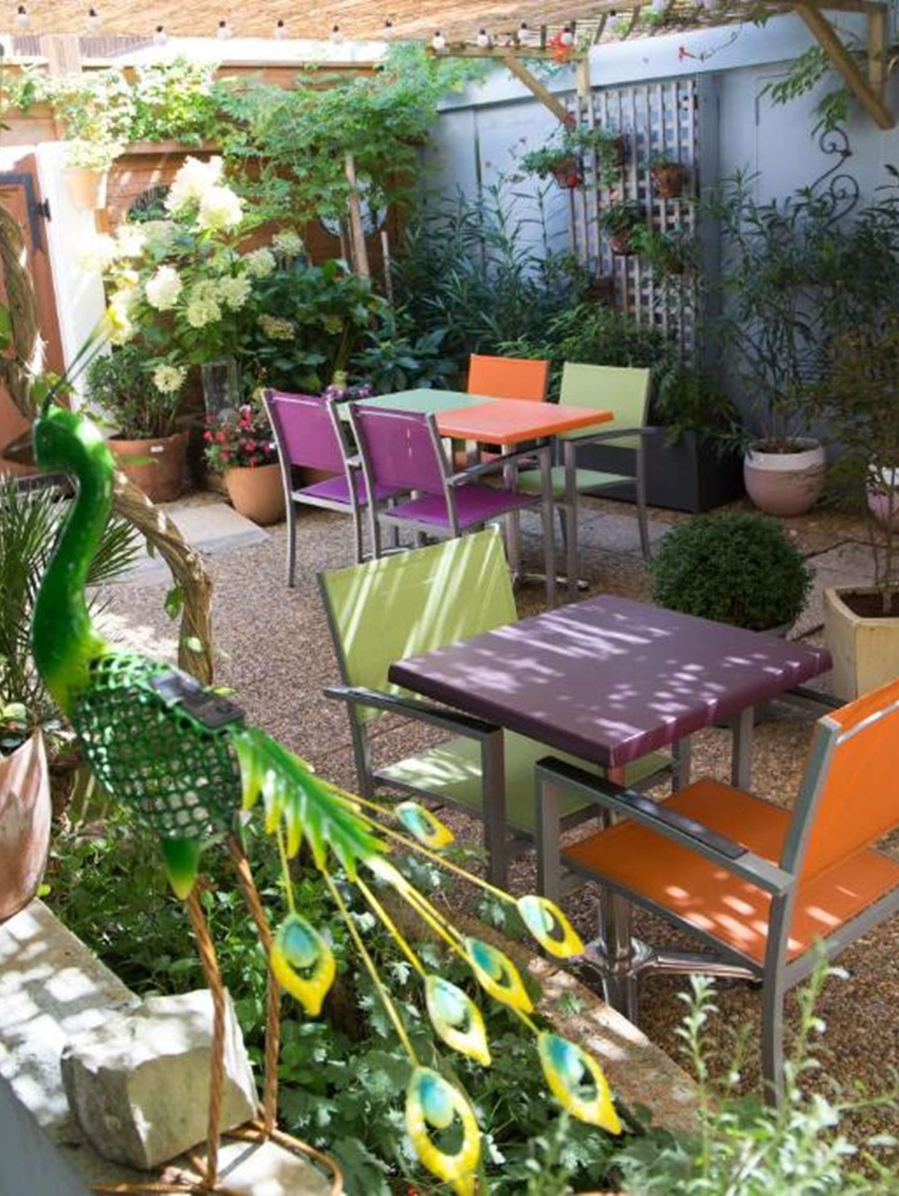 Eine Terrasse im Freien mit bunten Stühlen und Tischen, umgeben von Topfpflanzen und einer Pfauen-Anlage.