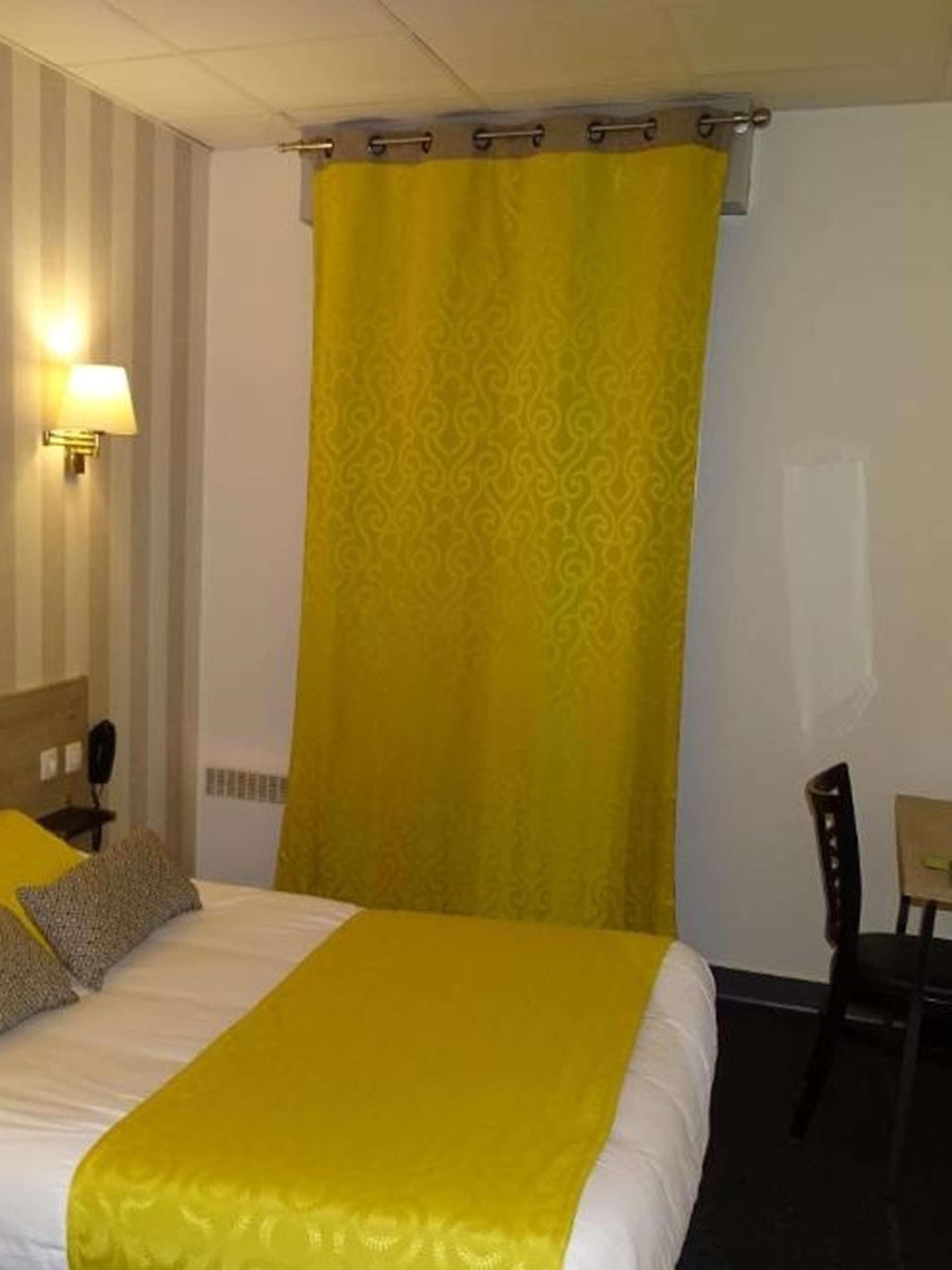 A hotel room with a bed, a nightstand, a lamp, a chair, and a curtain.