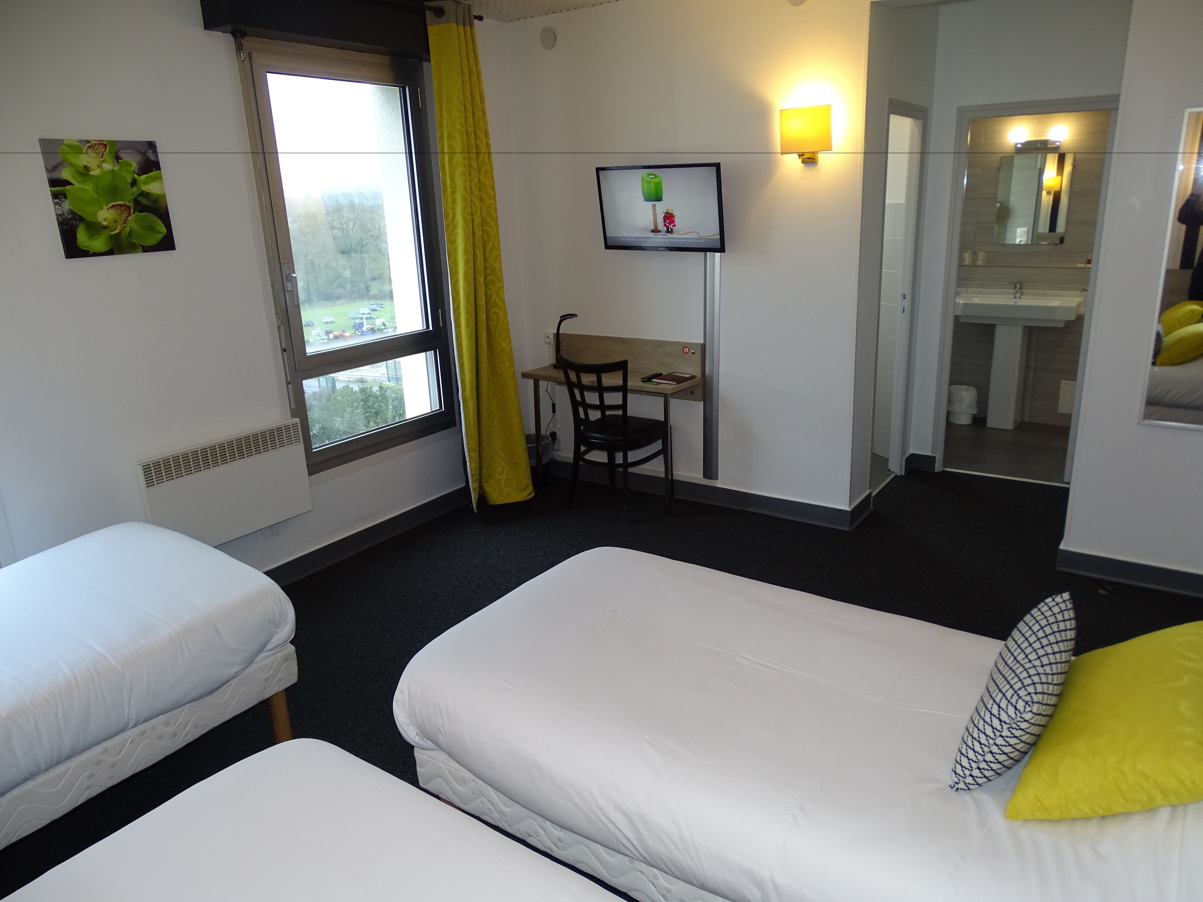 Habitación de hotel con dos camas individuales, un escritorio con silla, televisor y baño visible a través de una puerta abierta.
