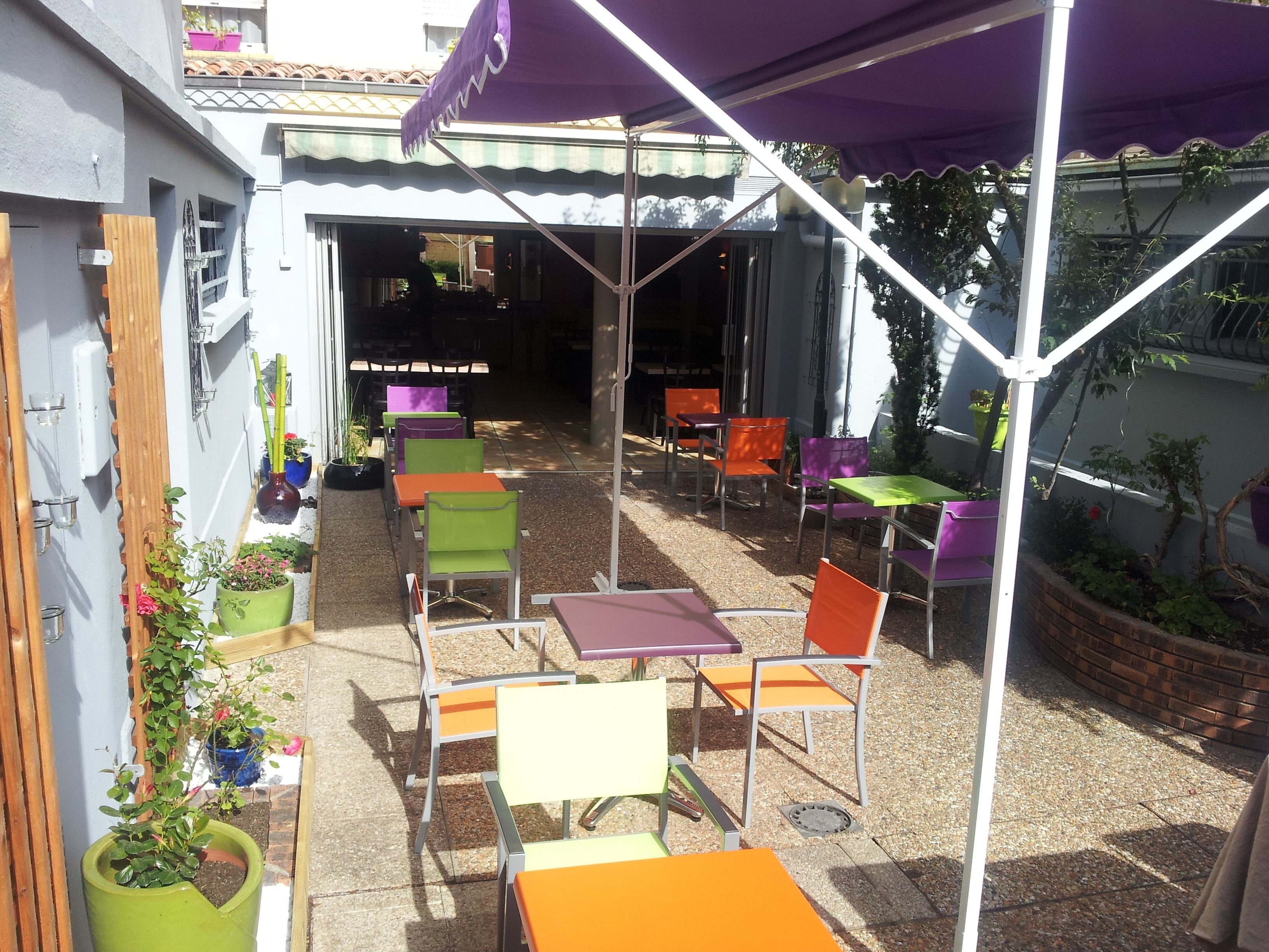 Un patio al aire libre con varias mesas y sillas, un espacio de estar cubierto y plantas en macetas.