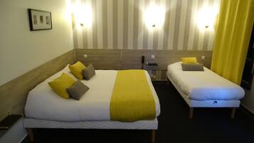 A hotel room with two beds, each with white bedding and yellow accents. There are two wall-mounted lights and a framed picture on the wall.