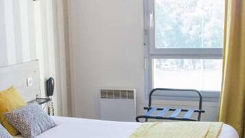 Una habitación de hotel con una cama, teléfono en la mesita de noche, ventana con cortinas y un radiador.