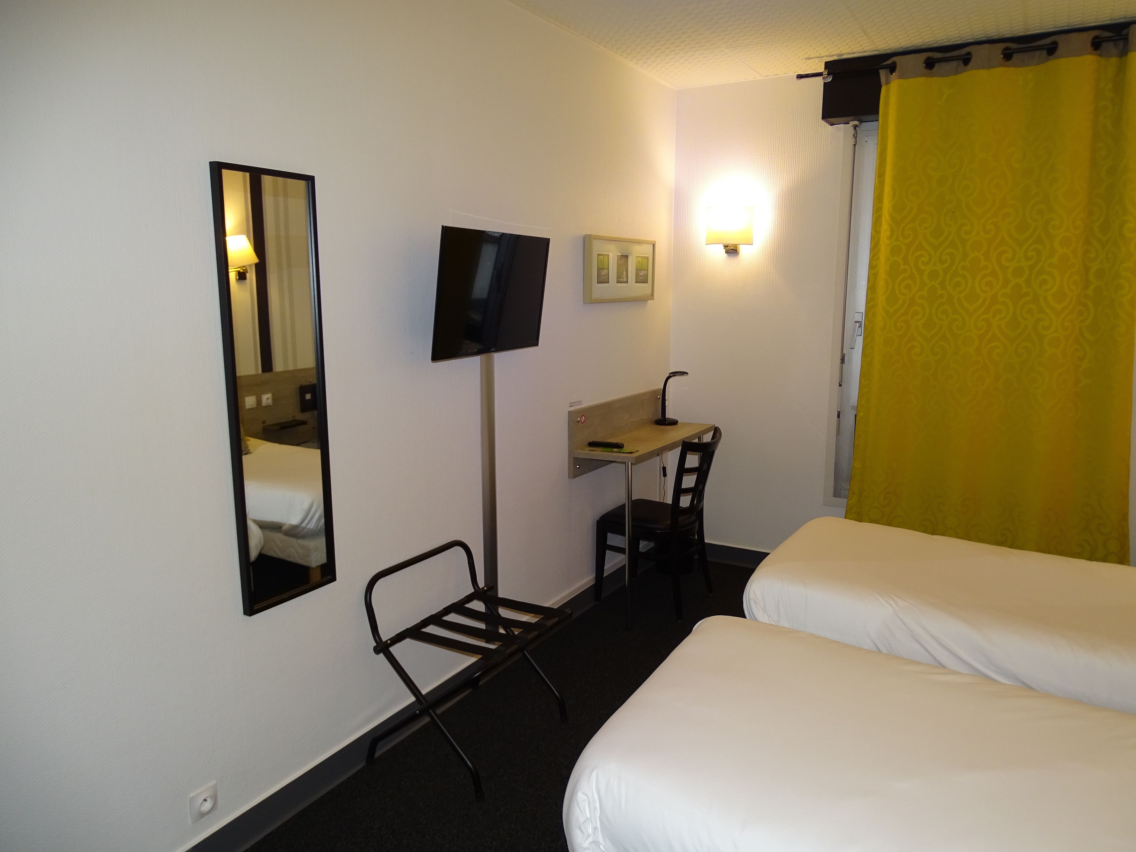 A hotel room with two beds, a desk with a chair, a television, and a mirror.
