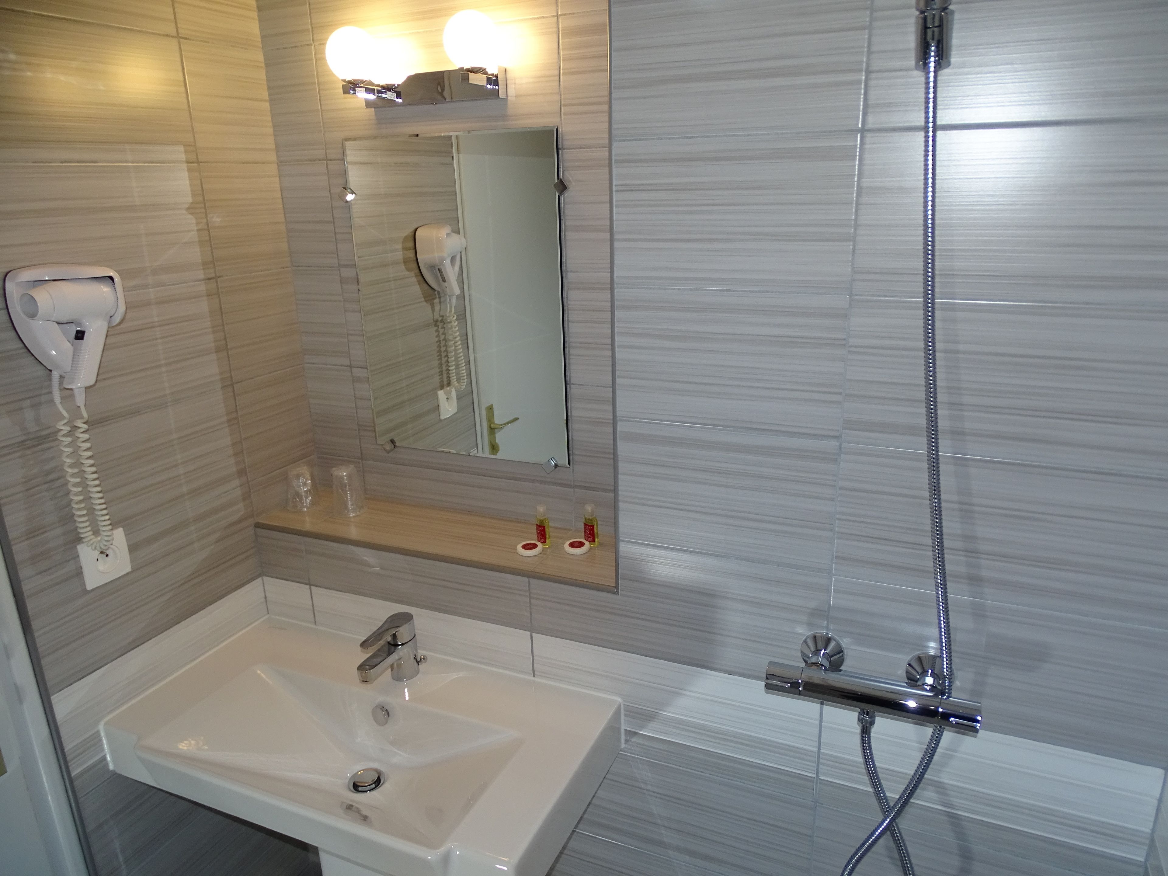 Un baño con lavamanos, espejo, secador de pelo y ducha.