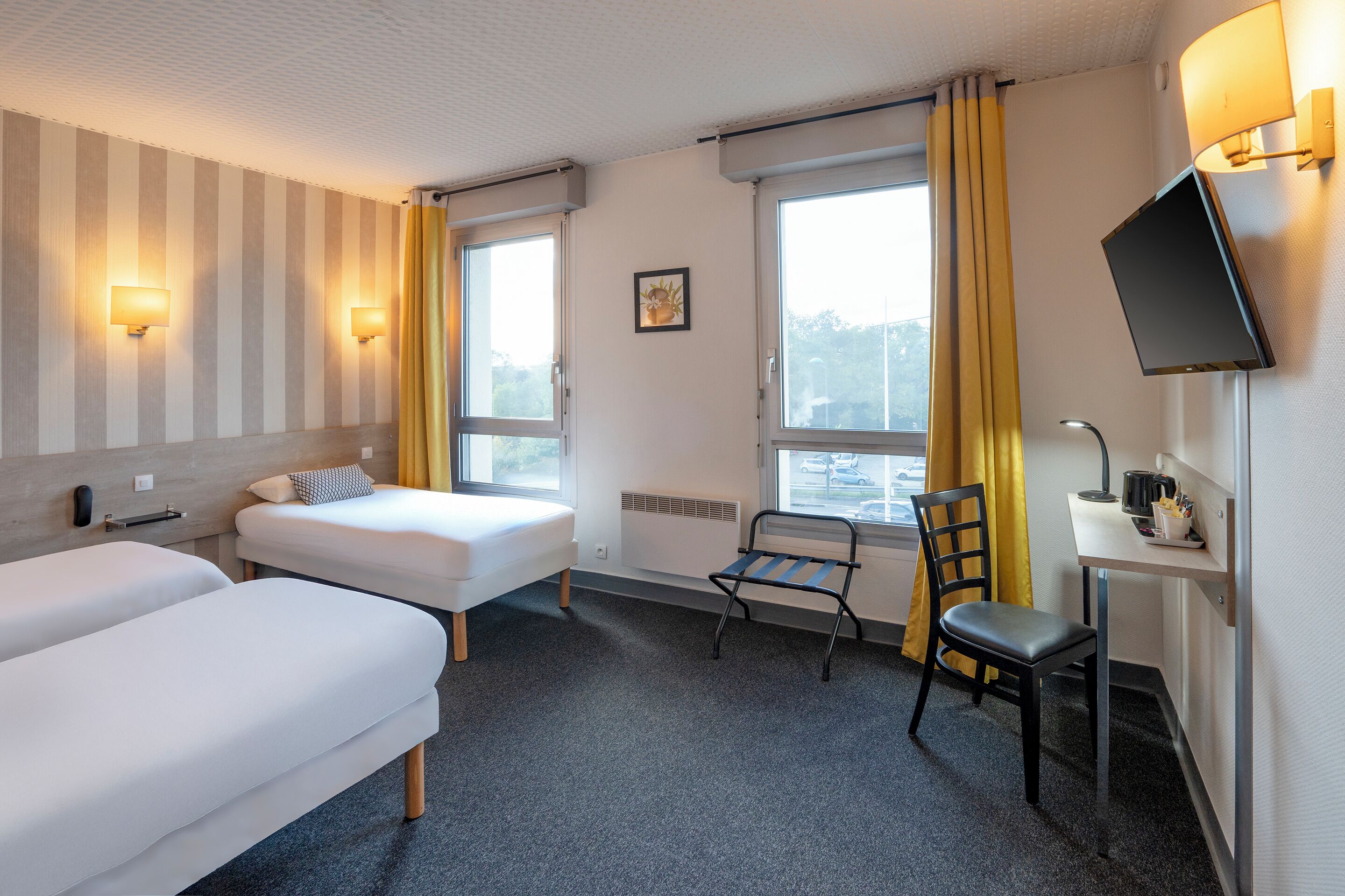 Hotelkamer met twee eenpersoonsbedden, een bureau met stoel, een televisie en een raam met gordijnen.