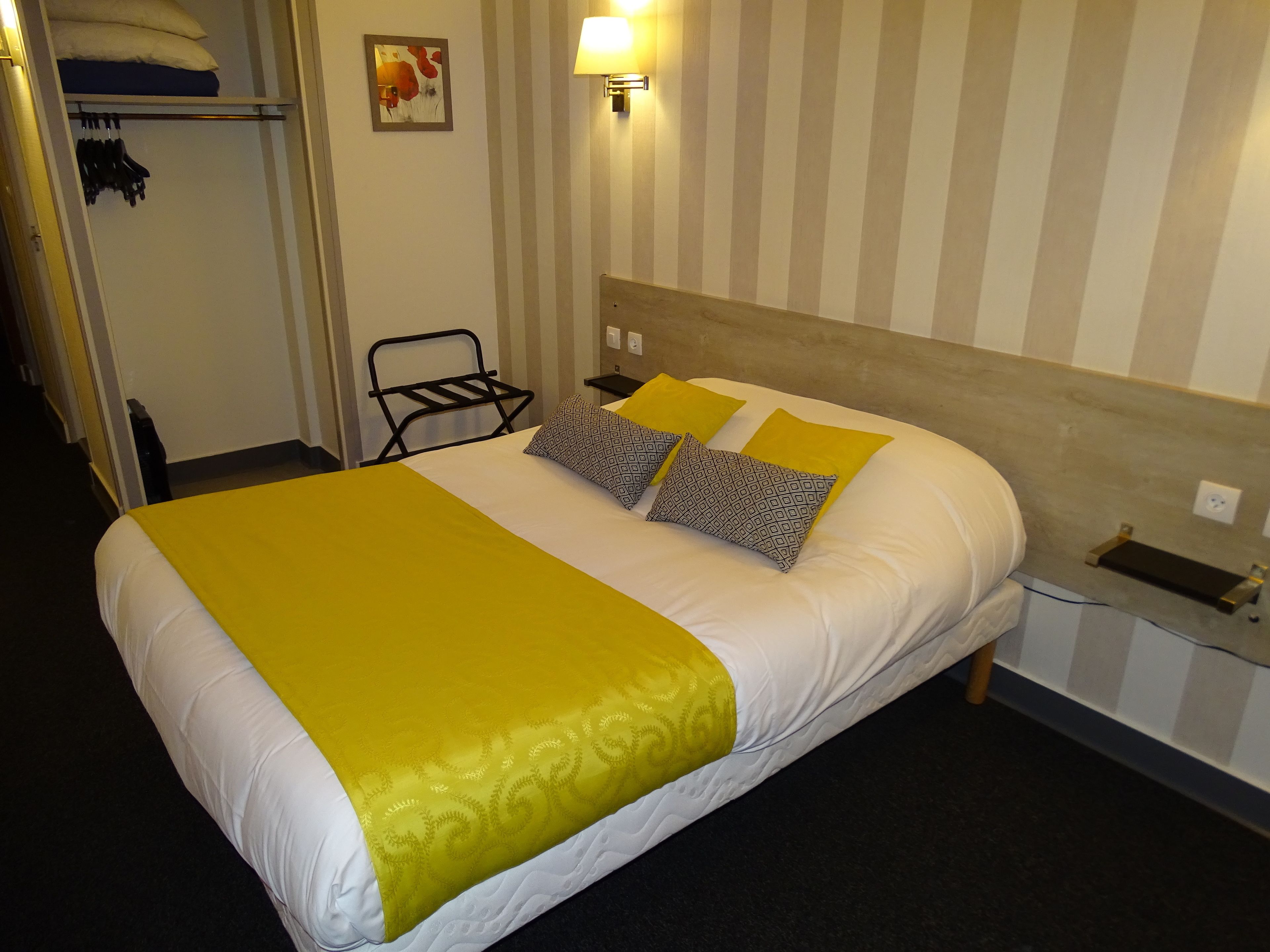 Une chambre d’hôtel comprenant un lit, une table de chevet, une lampe, une chaise et une armoire.