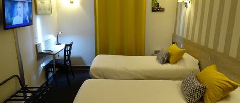 A hotel room with two beds, a desk, a chair, a TV, and a yellow curtain.