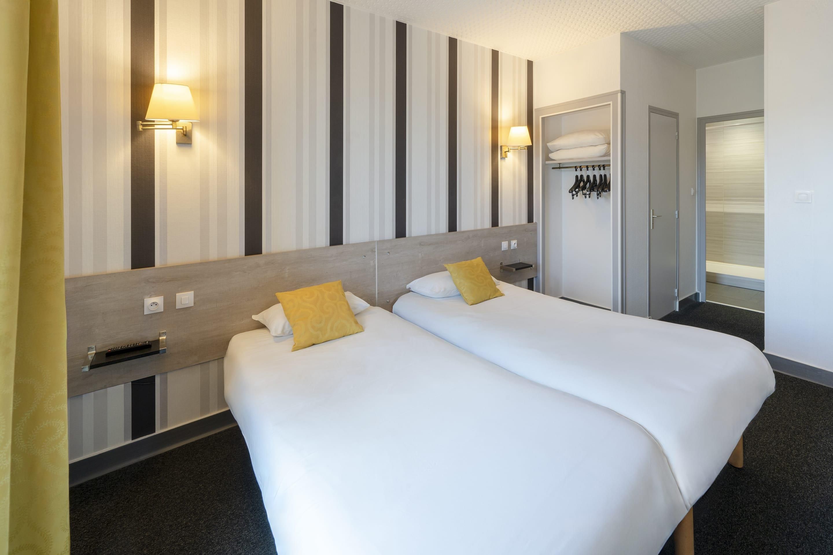 Habitación de hotel con dos camas, un armario, perchero y baño con ducha.