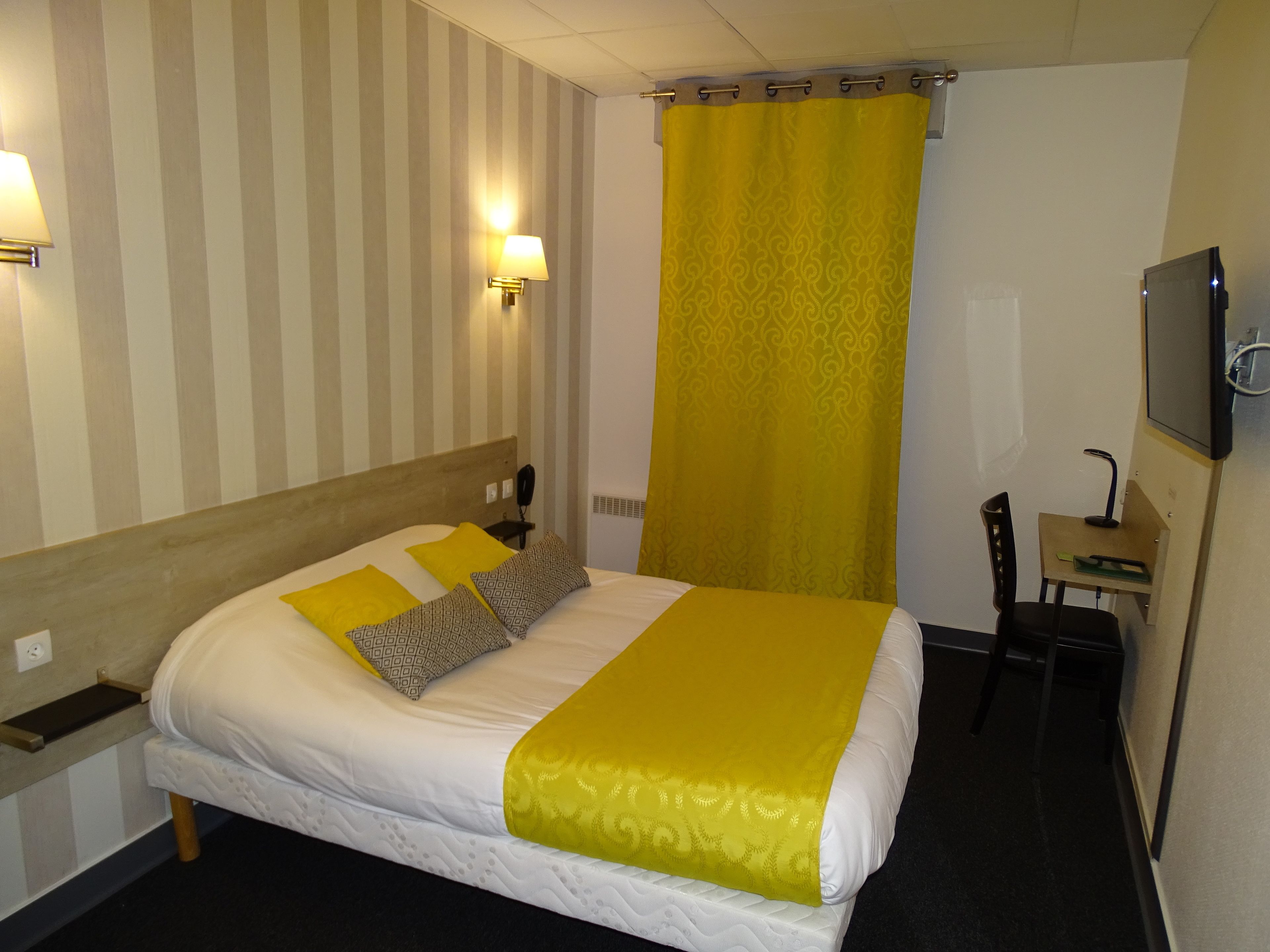 Una habitación de hotel con cama, dos lámparas de noche, un escritorio con silla y una televisión.