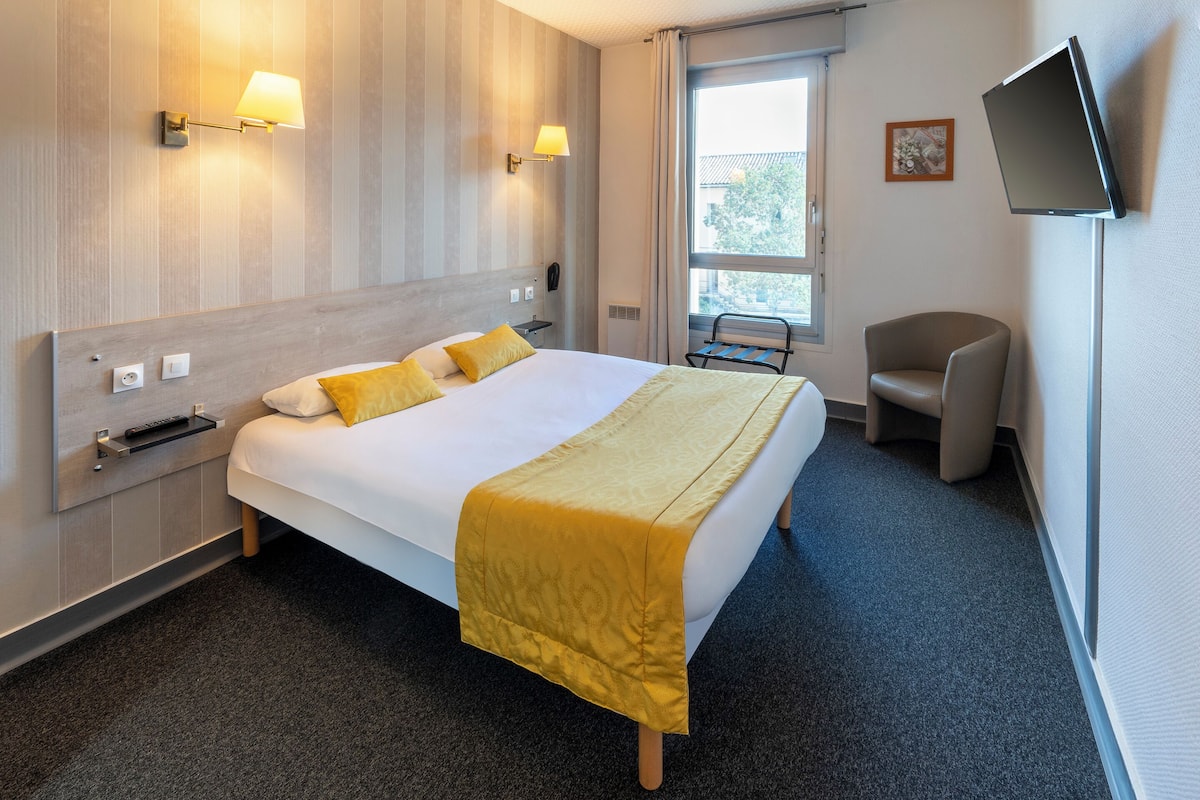 Ein Hotelzimmer mit einem großen Bett, Nachttischlampen, einem Flachbildfernseher, einem Sessel und einem Fenster mit Blick.