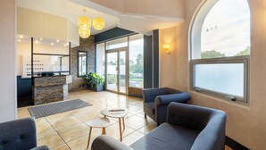 Un hall d’entrée moderne doté d’un comptoir de réception, d’un espace salon et de grandes fenêtres offrant une vue sur l’extérieur.