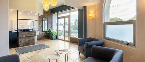 Un lobby moderno con mostrador de recepción, zona de estar y ventanas amplias que ofrecen vistas al exterior.