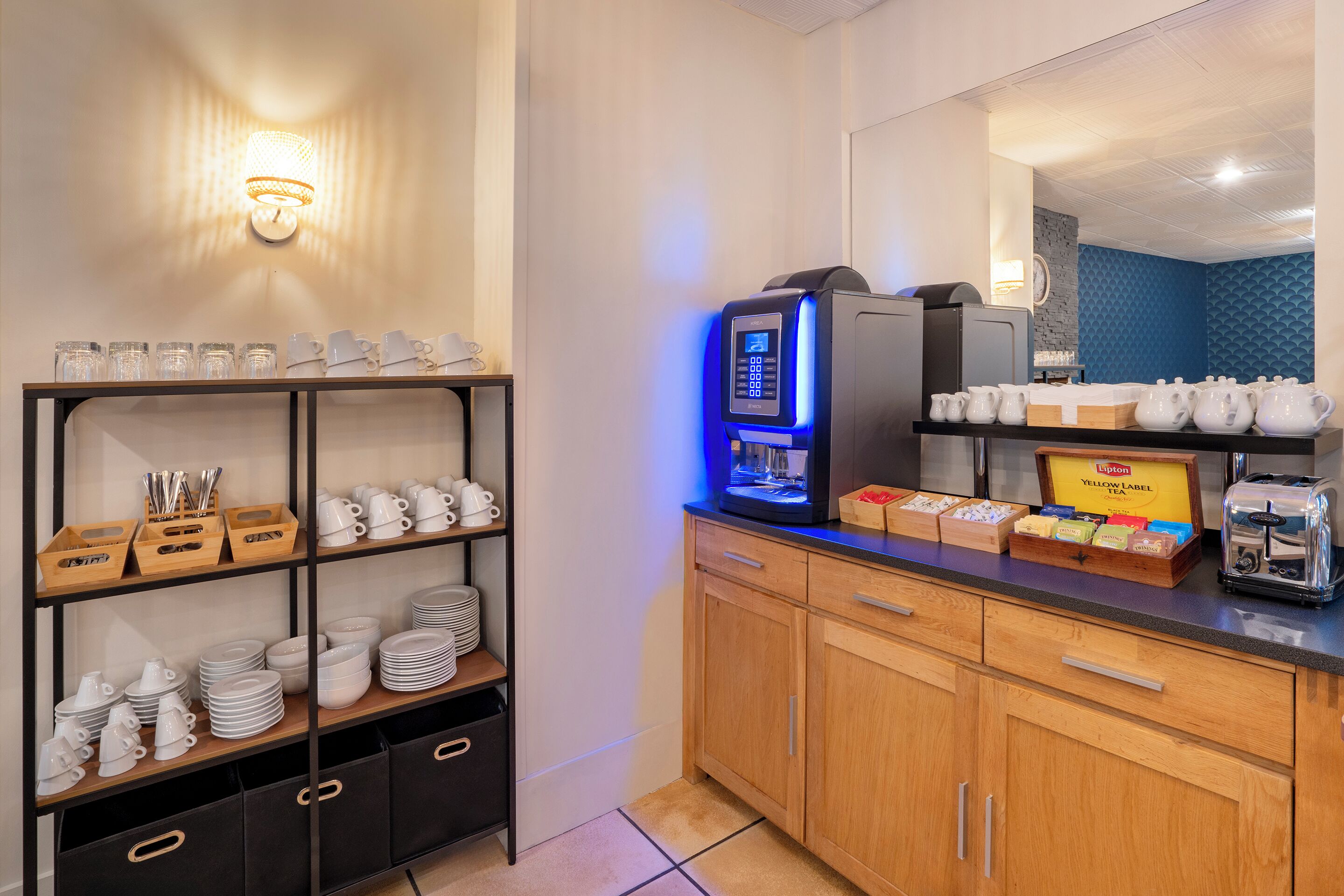 Una cocina de hotel con una máquina de café, un espacio para el té y utensilios de cocina ordenados.