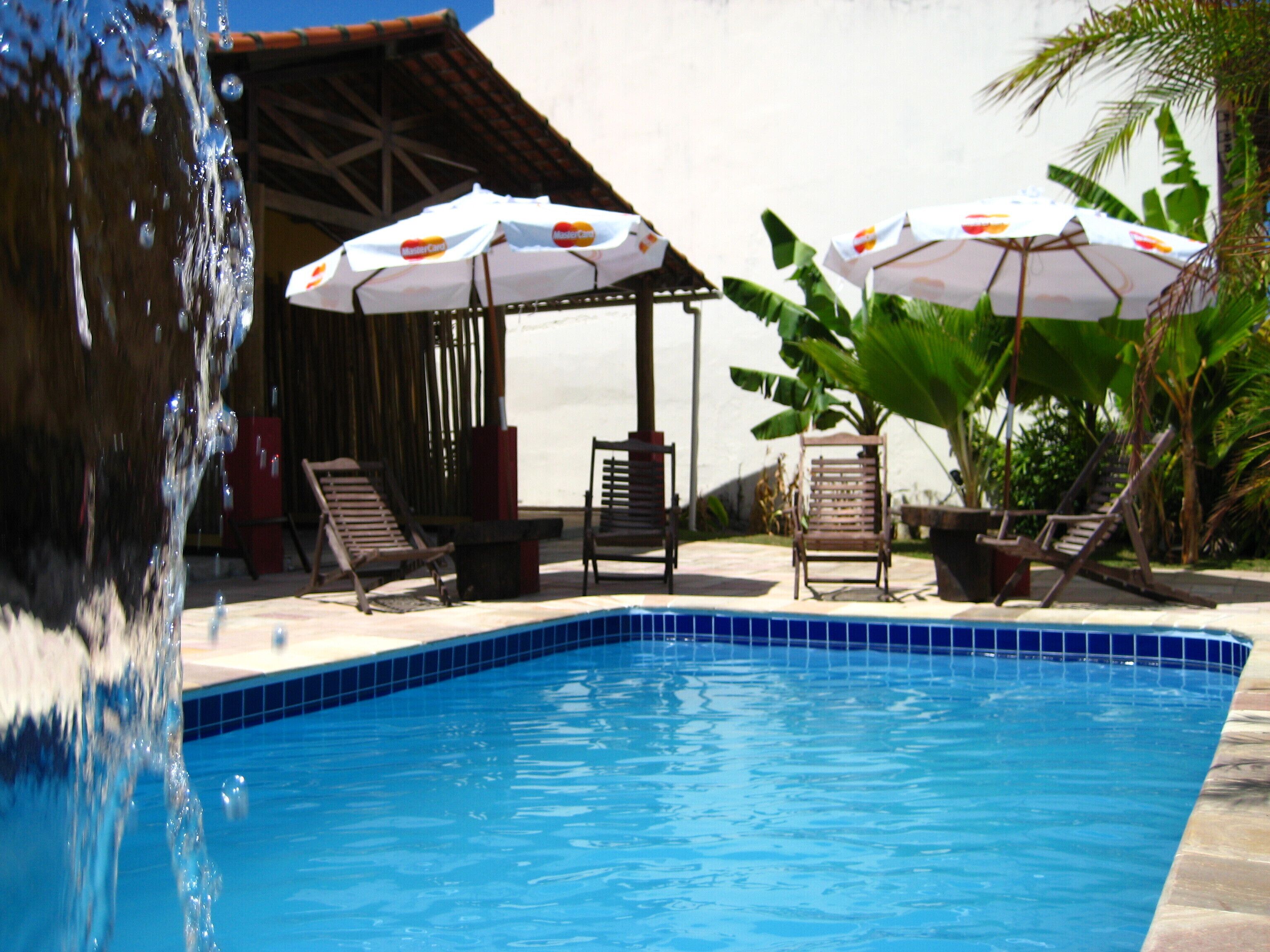 A swimming pool with a clear blue water edge, surrounded by lounge chairs and umbrellas.