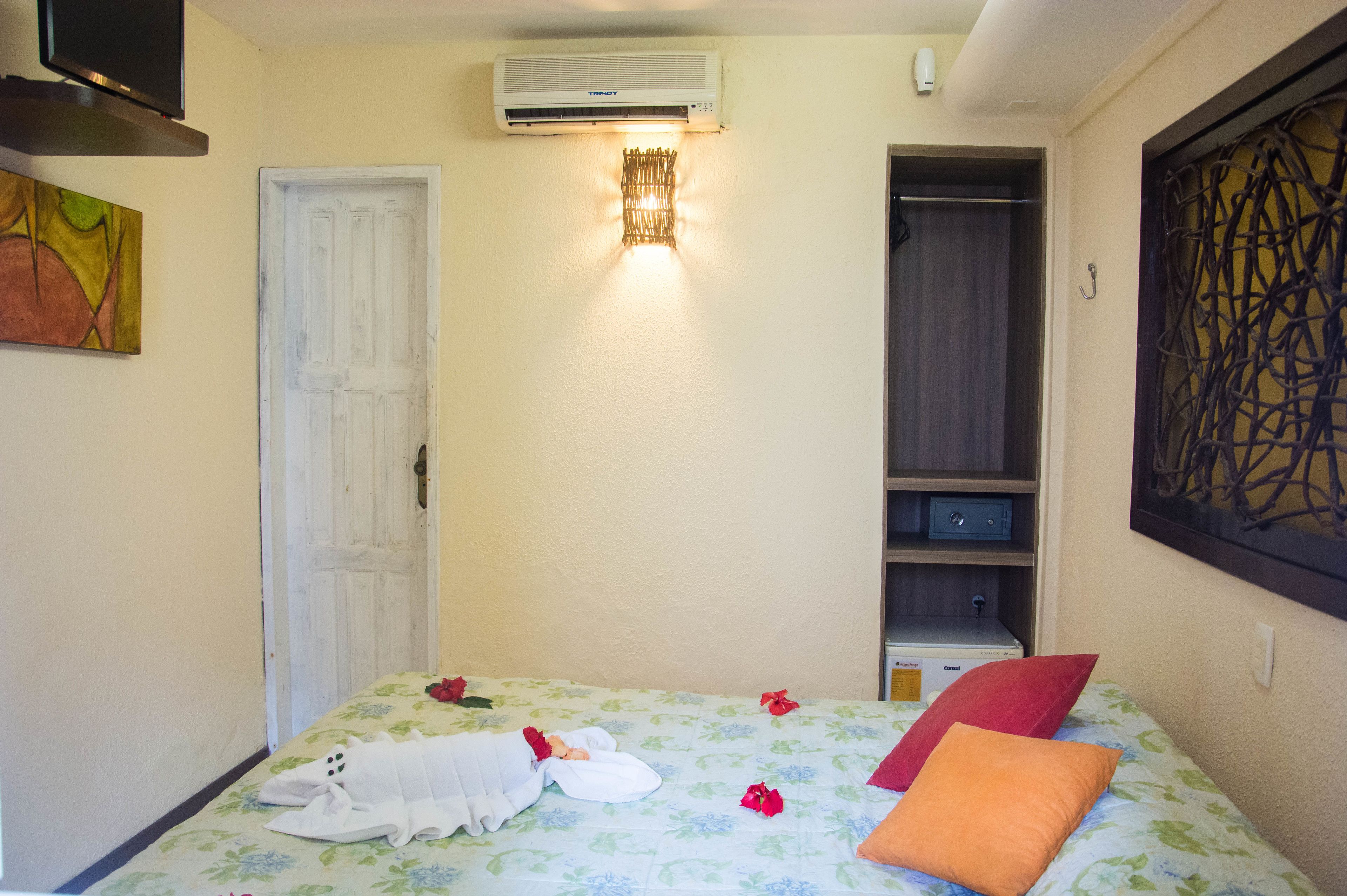 A hotel room with a bed, a wardrobe, an air conditioning unit, and a wall-mounted light fixture.