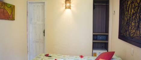 A hotel room with a bed, a wardrobe, an air conditioning unit, and a wall-mounted light fixture.