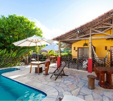 A pool area with a stone floor, wooden lounge chairs, and umbrellas.
