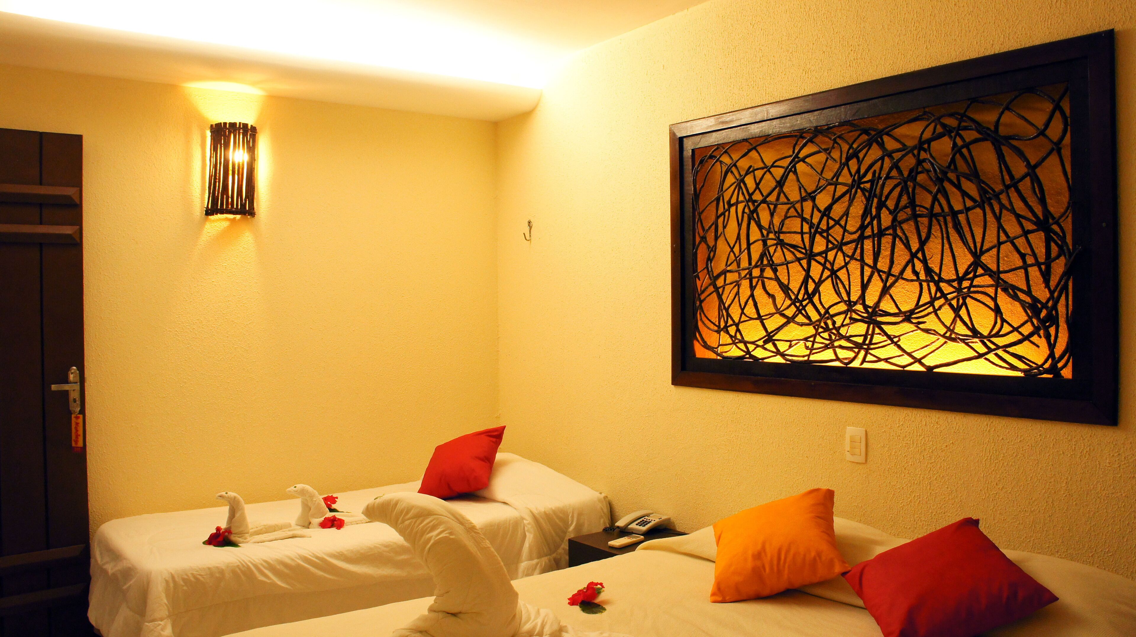 Une chambre d’hôtel avec deux lits, une œuvre d’art accrochée au mur, une table de chevet avec un téléphone et un luminaire fixé au mur.