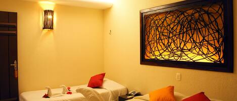 A hotel room with two beds, a wall-mounted artwork, a bedside table with a phone, and a wall-mounted light fixture.