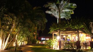 A nighttime view of a resort with a well-lit gazebo, palm trees, and a building with illuminated windows. - Hotel Aconchego Porto de Galinhas (Ipojuca)