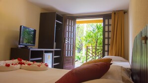 A hotel room with a bed, a television, a wardrobe, and a balcony with a view of greenery. - Hotel Aconchego Porto de Galinhas (Ipojuca)